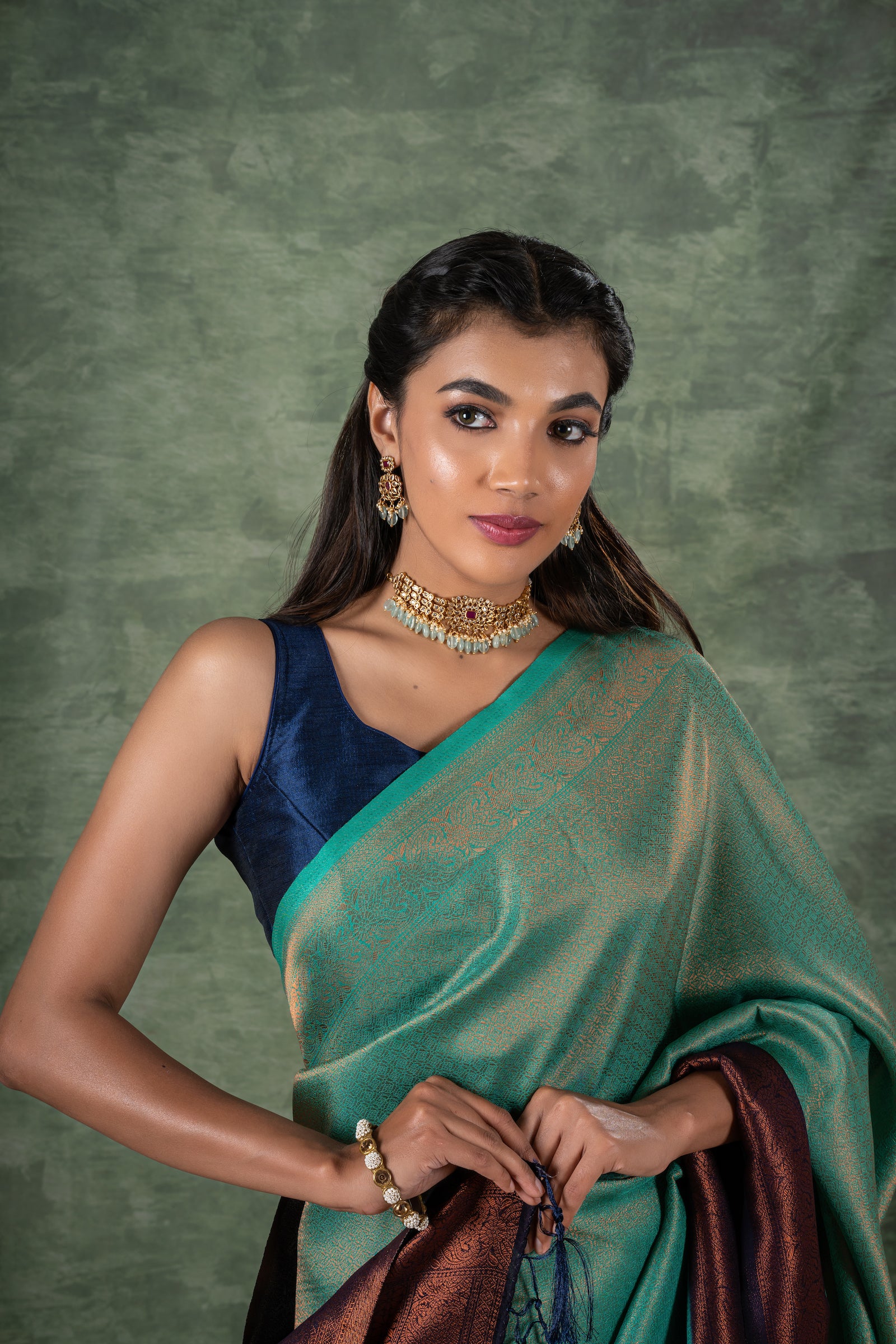 A model of le pleat draped in a lightweight banana's art silk saree with a sleeveless blue raw silk blouse and dark blue saree shaper and Amira necklace set.