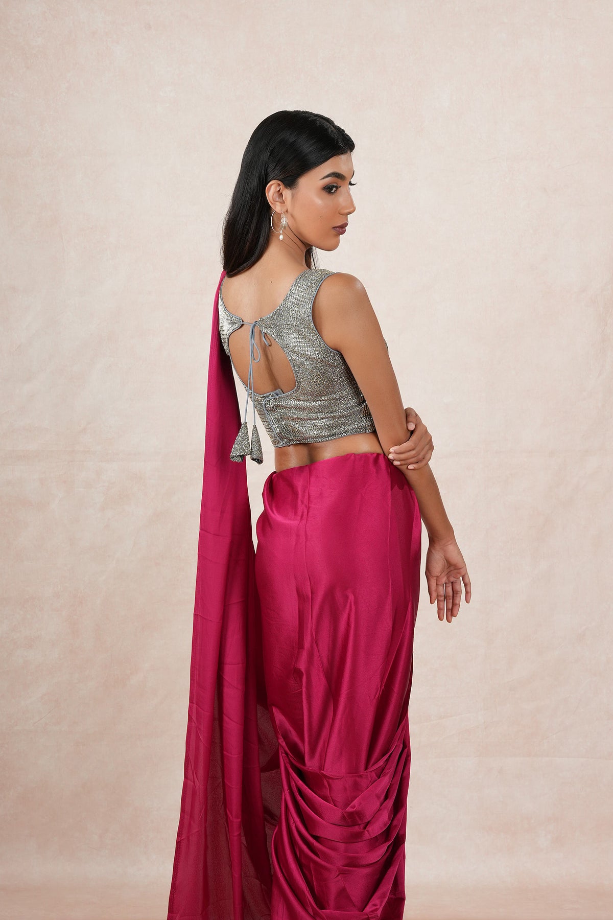 A model draped in a dark pink satin silk saree, grey shimmer blouse and maroon saree shaper. The saree is pleated and  held with a waist chain.