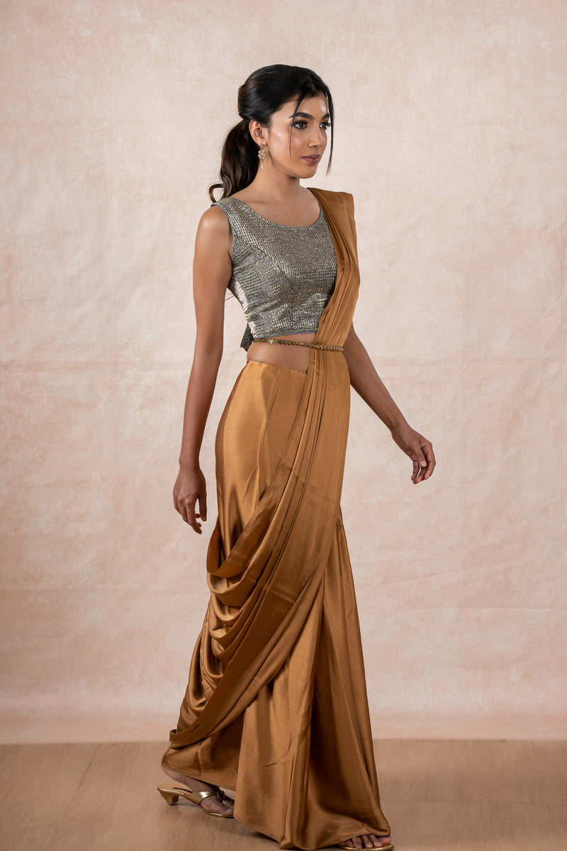 A model draped in a copper brown satin silk saree, grey shimmer blouse and gold buff saree shaper. The saree is pleated and  held with a waist chain.