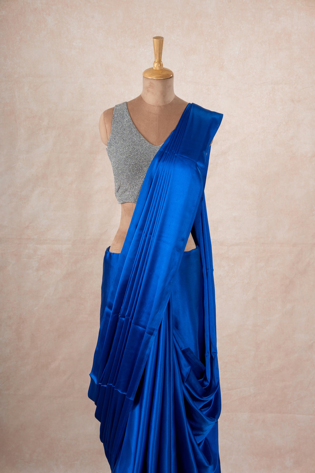 A mannequin draped in a dark blue satin silk saree, grey glitter blouse and dark blue saree shaper. The saree is pleated beautifully around the shoulder.