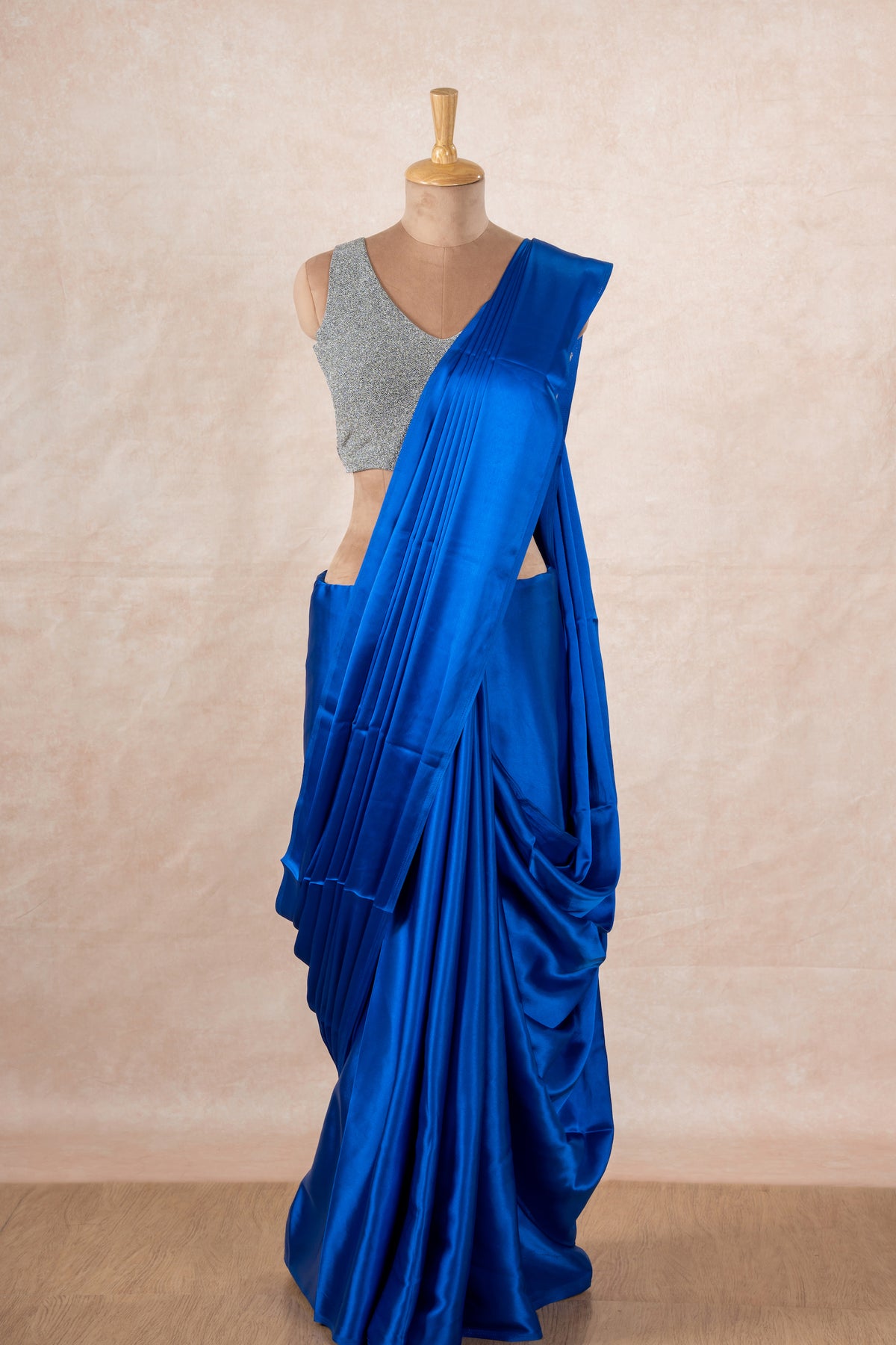 A mannequin draped in a dark blue satin silk saree, grey glitter blouse and dark blue saree shaper. The saree is pleated beautifully around the shoulder.