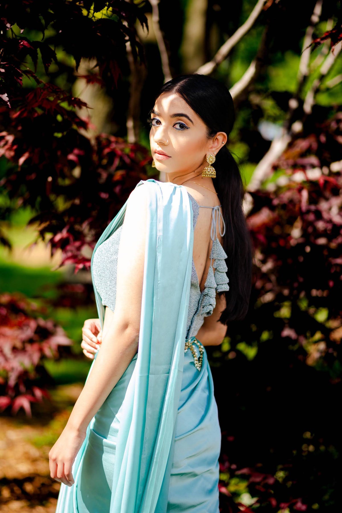 A model draped in an aqua blue satin silk saree, grey shimmer blouse and light blue saree shaper. The saree is pleated and  held with a waist chain.