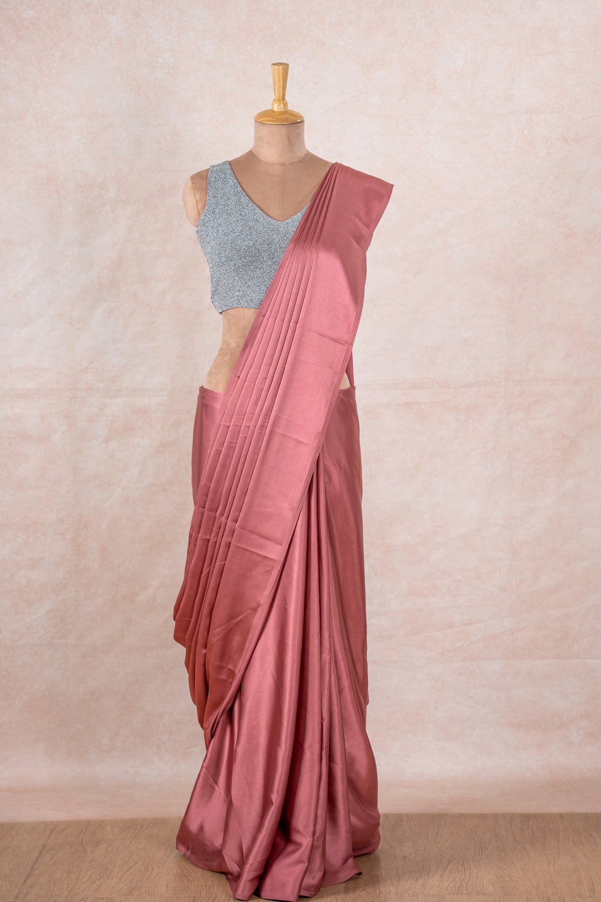 A mannequin draped in a pale pink satin silk saree, grey shimmer blouse and gold buff shaper. The saree is pleated beautifully around the shoulder.