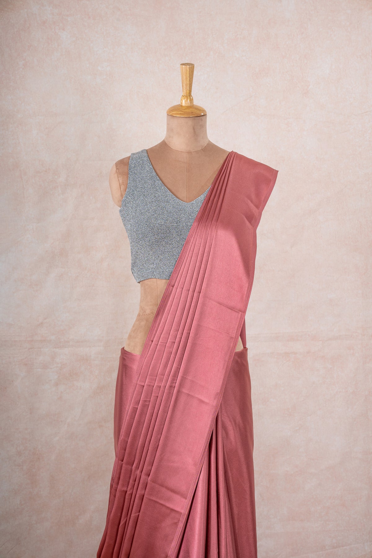 A mannequin draped in an pale pink satin silk saree, grey shimmer blouse and gold buff shaper. The saree is pleated beautifully around the shoulder.