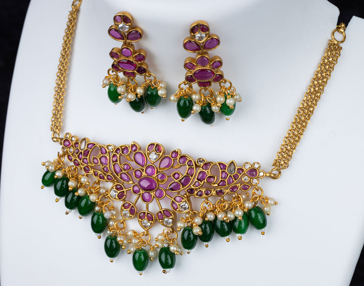 An elegant necklace set in peacock design with pink kundan stone and green beads, and matching earrings