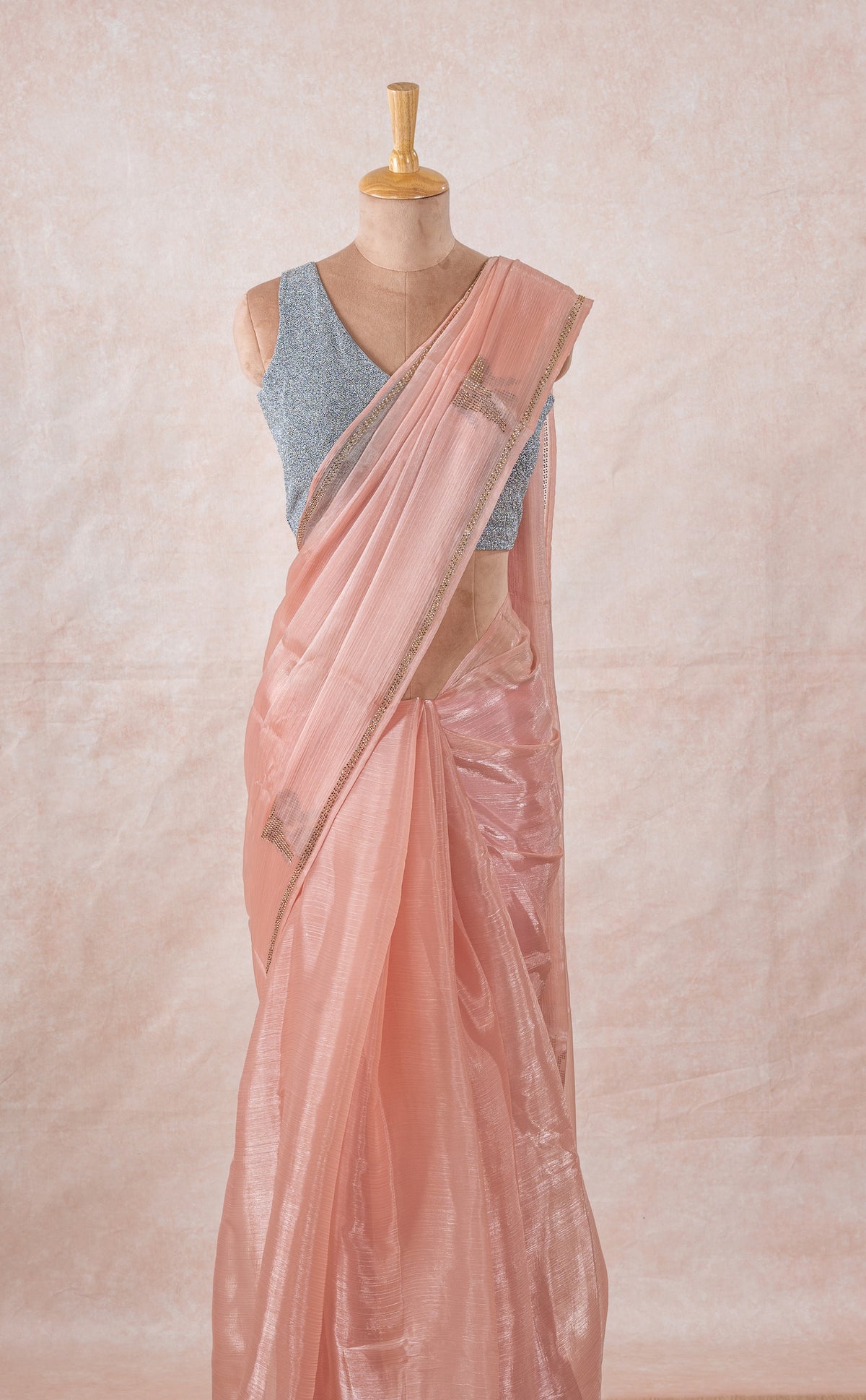 A mannequin draped in a sheer lightweight pink chinon chiffon saree with imitation swarovski stone crystal embellishments, sleeveess grey glitter blouse and pink blush saree shaper