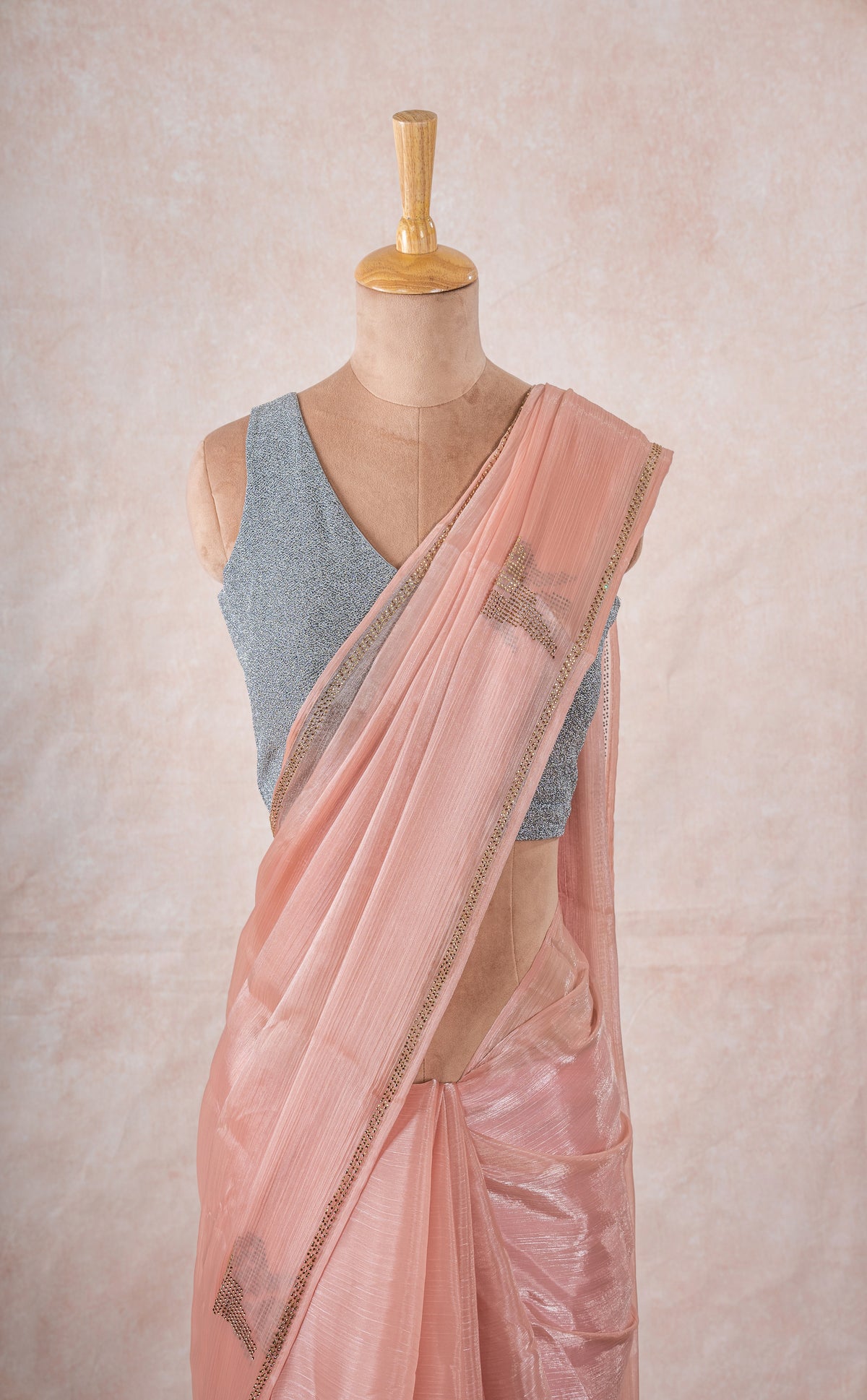 A mannequin draped in a sheer lightweight pink chinon chiffon saree with imitation swarovski stone crystal embellishments, sleeveess grey glitter blouse and pink blush saree shaper