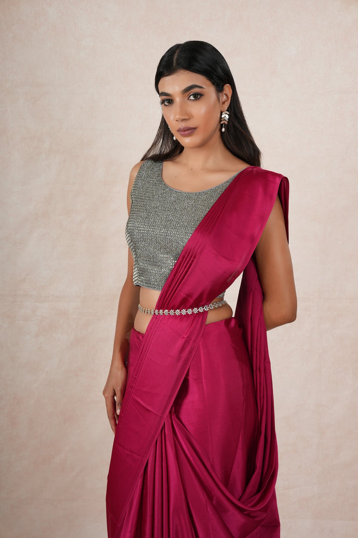 A model draped in a dark pink satin silk saree, grey shimmer blouse and maroon saree shaper. The saree is pleated and  held with a waist chain.