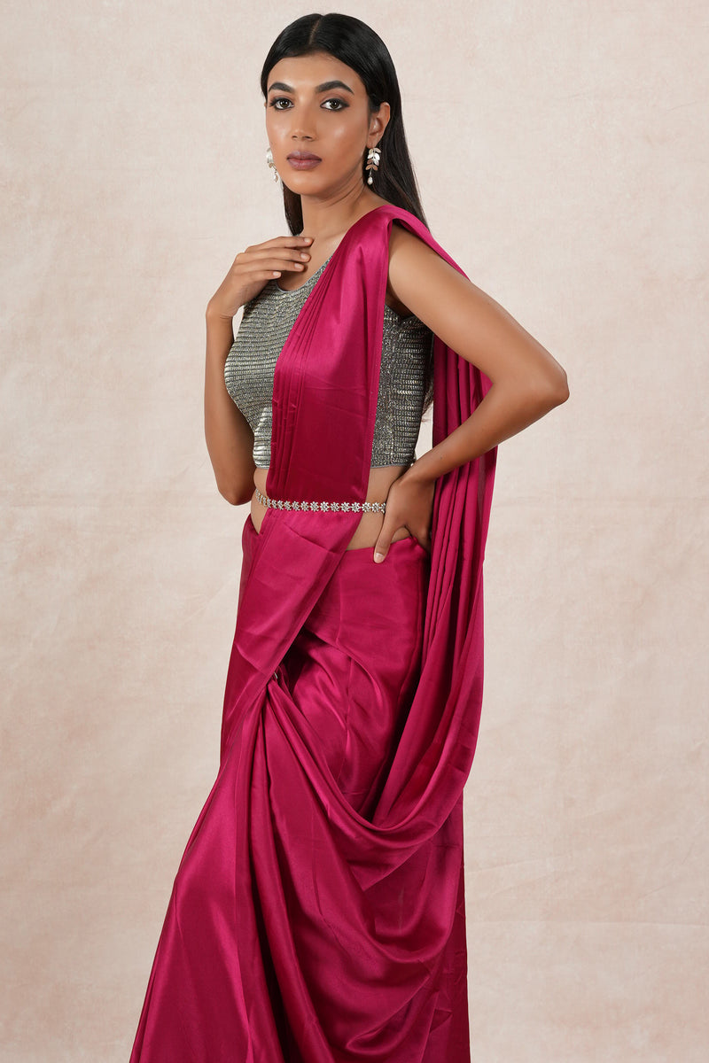 A model draped in a dark pink satin silk saree, grey shimmer blouse and maroon saree shaper. The saree is pleated and  held with a waist chain.