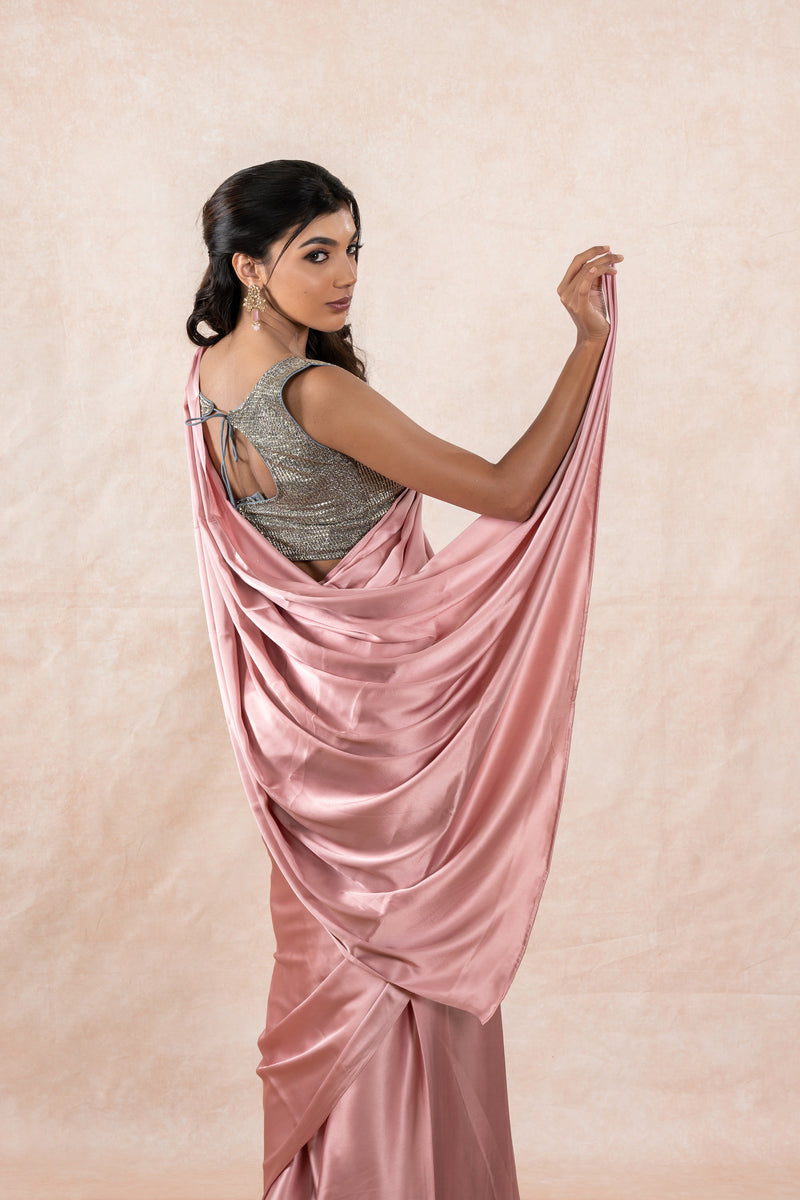 A model draped in a light pink satin silk saree, grey glitter blouse and light pink shaper. The saree is pleated beautifully around the shoulder.