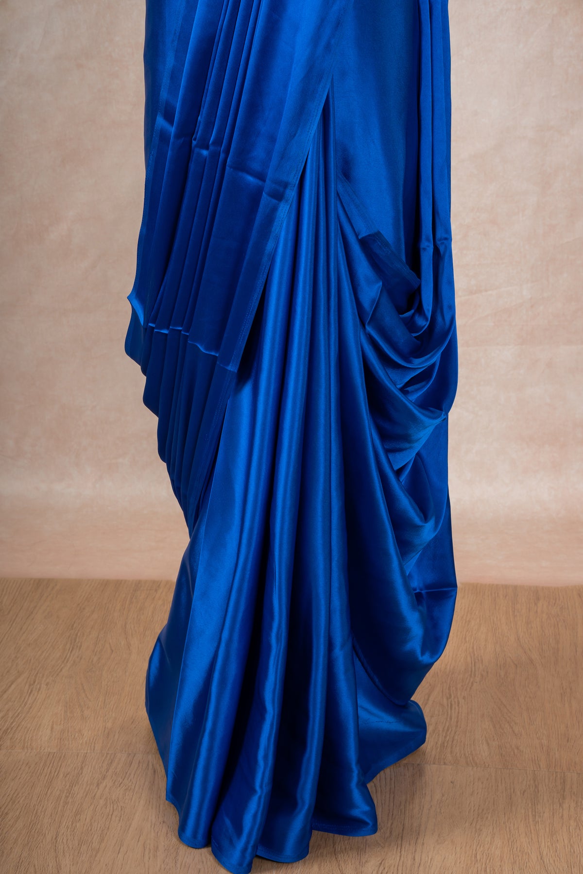 A mannequin draped in a dark blue satin silk saree, grey glitter blouse and dark blue saree shaper. The saree is pleated beautifully around the shoulder.