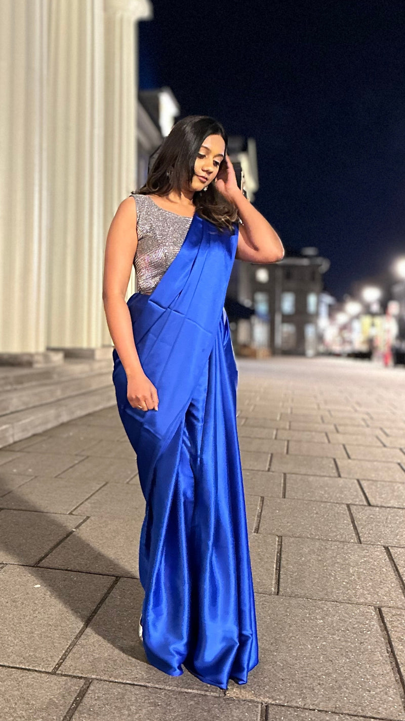 A model draped in a dark blue satin silk saree, grey glitter blouse and dark blue saree shaper. The saree is pleated beautifully around the shoulder.