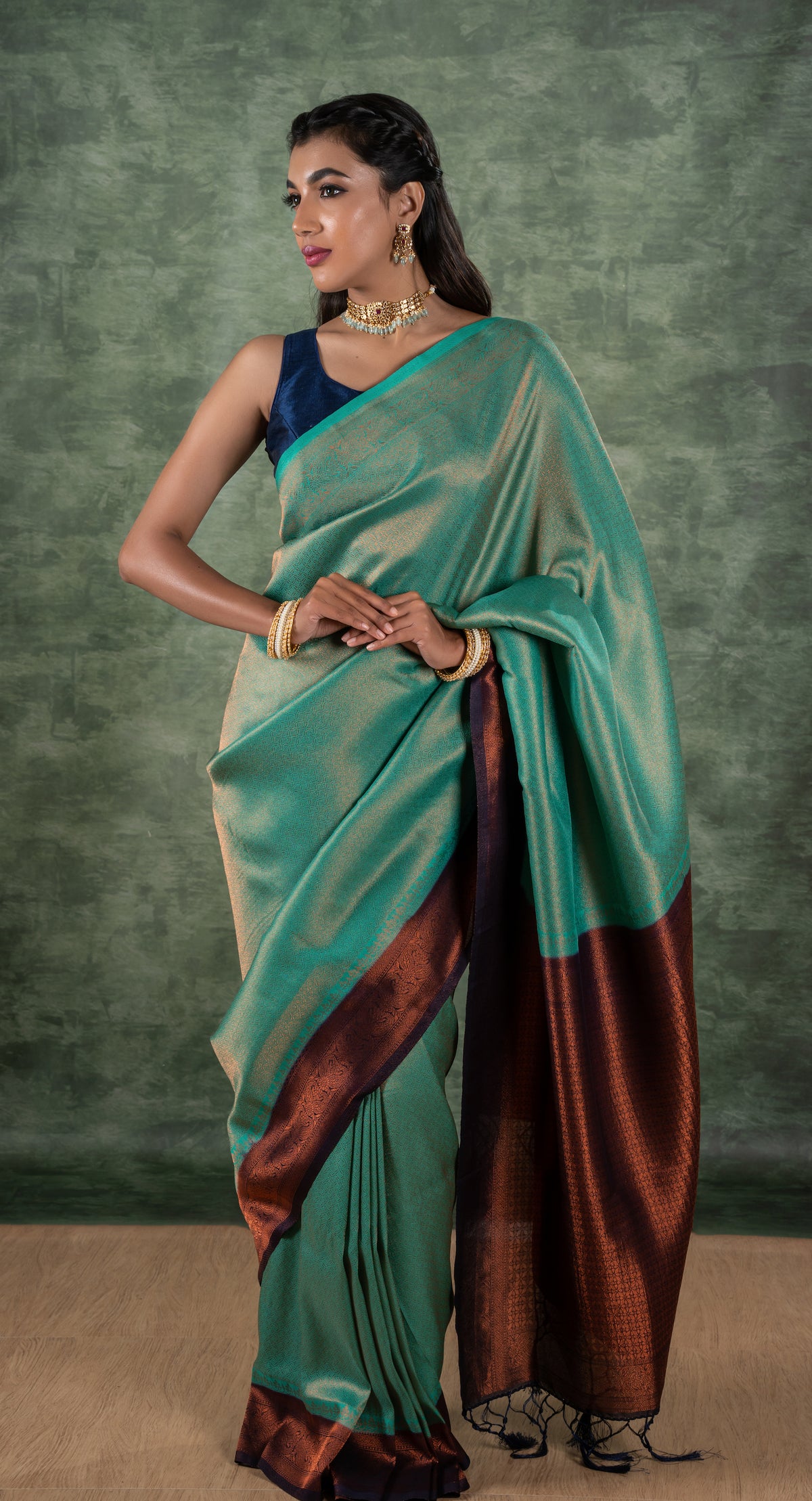 A model of le pleat draped in a lightweight banana's art silk saree with a sleeveless blue raw silk blouse and dark blue saree shaper and Amira necklace set.