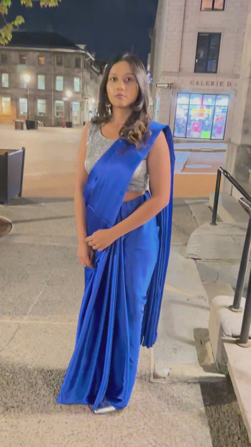 A model draped in a dark blue satin silk saree, grey glitter blouse and dark blue saree shaper. The saree is pleated beautifully around the shoulder.