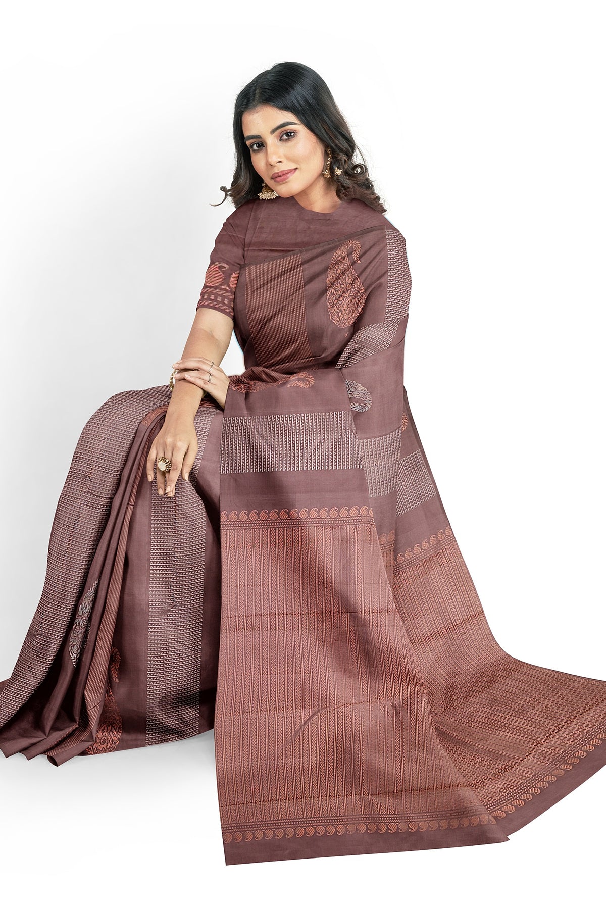 A model draped in  a unique and rich brown soft silk handloom saree with brown body and  pallu. The saree is designed with paisley & geometrical motifs in silver & copper zari works. The saree comes with an attached running blouse.